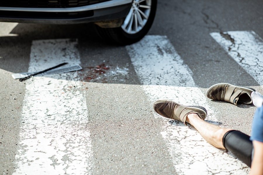 Injured pedestrian lying on a crosswalk after being hit by a car, with blood, broken license plate, and a shoe scattered on the road.