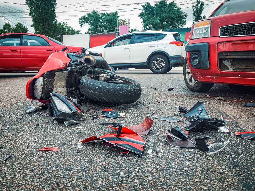A red motorcycle lays in pieces, badly damaged, on a road after an accident.