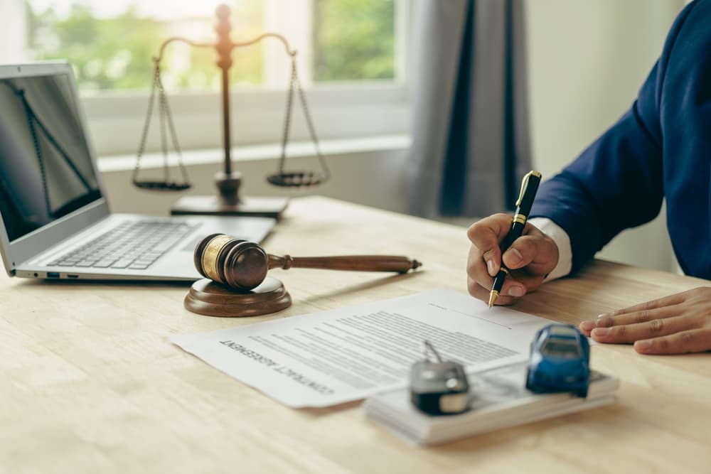 A lawyer, judge's gavel, and miniature car symbolize court action or auction following a car accident and insurance payout. Discover the legal implications.