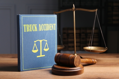 A law book labeled "Truck Accident" beside a gavel and scales of justice on a wooden desk, symbolizing legal action after a trucking crash.